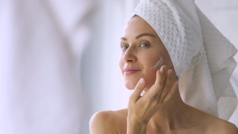 A woman applies skincare cream to her face, practicing smart skincare to combat skin aging