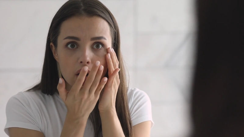 A woman looks at her reflection, concerned about the effects of stress on skin aging