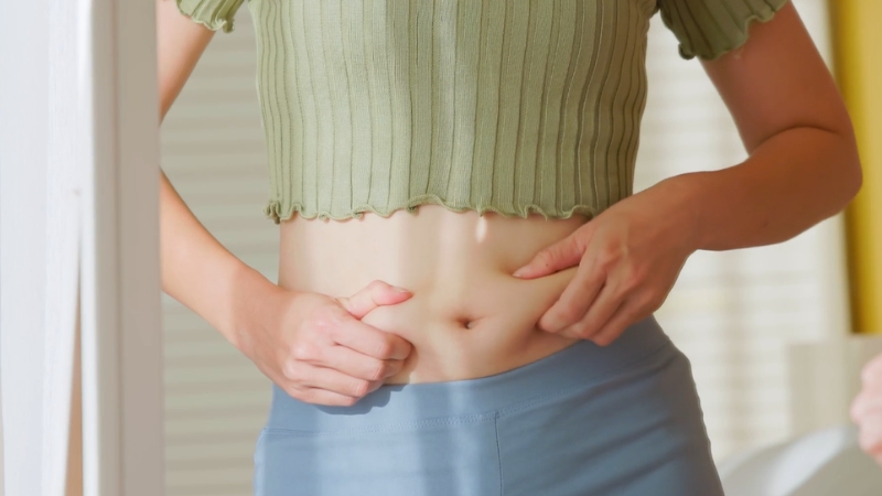 Image of a woman examining her abdominal area, which may be linked to hormone-related fat gain