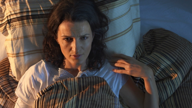 A woman lying awake in bed, looking frustrated and unable to sleep during the night