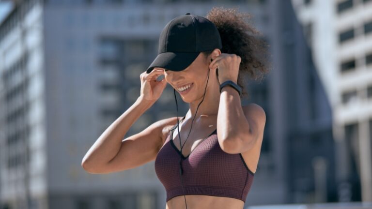 Woman smiling outdoors while adjusting earphones after a workout, showing a natural way to boost mood without sugar or caffeine