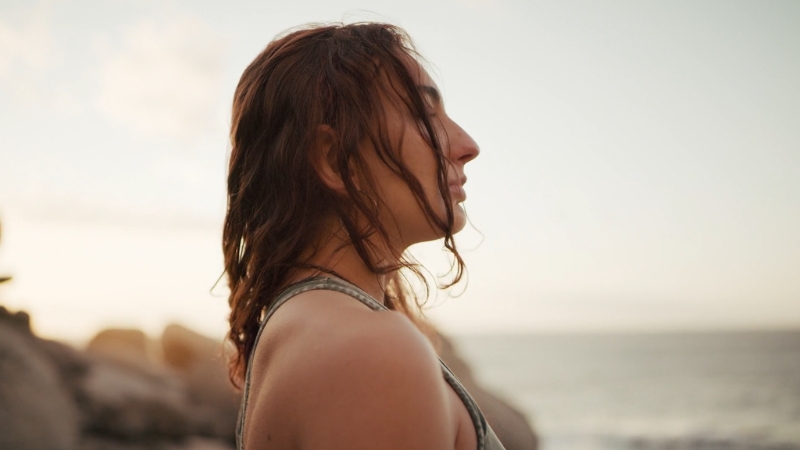 Woman standing by the ocean with eyes closed, using breathwork and mindfulness to boost mood naturally