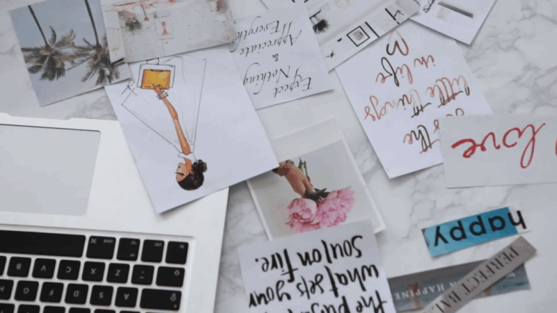 Printed photos, quotes, and cut-out words scattered next to a laptop, ready to be used for a personal vision board
