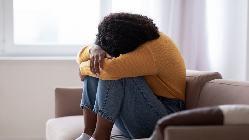 Woman sitting on couch with head down shows emotional and physical toll of overlooked postpartum complications
