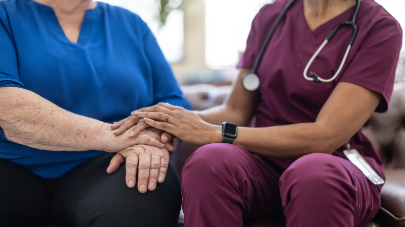 A nurse holds an elderly woman's hands, showing care for women in nursing homes