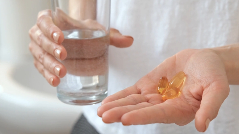 A person holds natural supplement capsules and a glass of water to support relief from chronic back discomfort