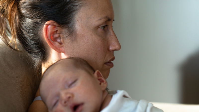 Mother holding newborn looks tired, showing missed postpartum symptoms