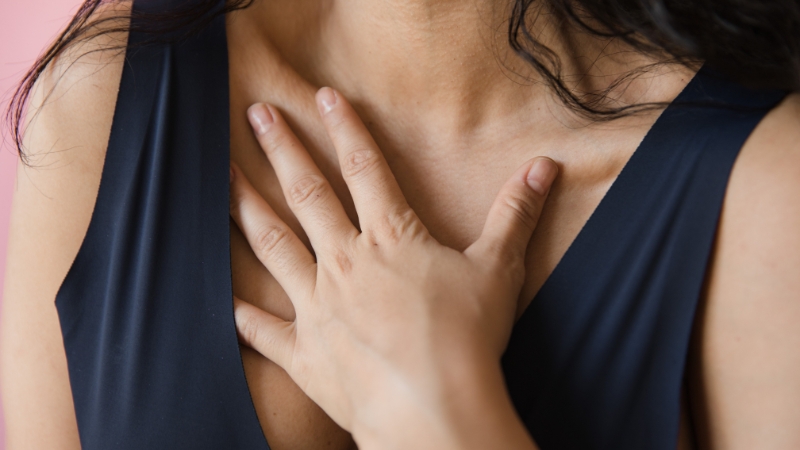 A woman in a sleeveless navy top gently rests her hand on her chest