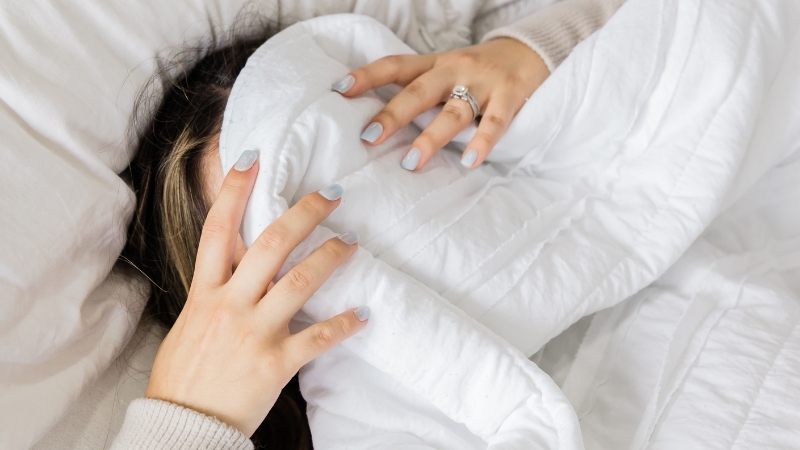 Woman hiding under a white blanket, showing signs of exhaustion linked to poor sleep and hormone imbalance
