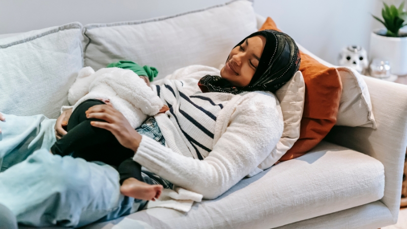Mother resting with baby shows how postpartum care differs by race and income