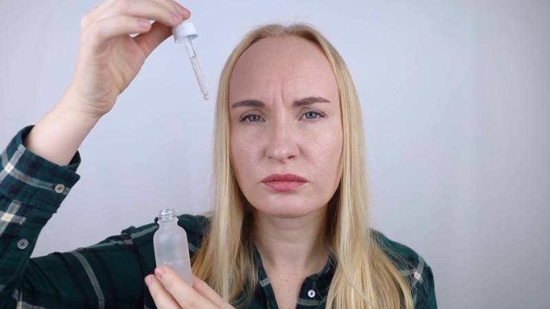 A woman holds a nearly empty retinol dropper bottle and looks concerned about its quality