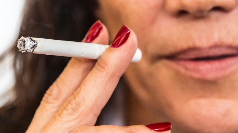 A close-up of a woman holding a lit cigarette near her mouth, highlighting smoking’s impact on hair health