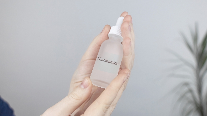A person holds a clear bottle of niacinamide serum, illustrating the question “does niacinamide expire” about skincare shelf life