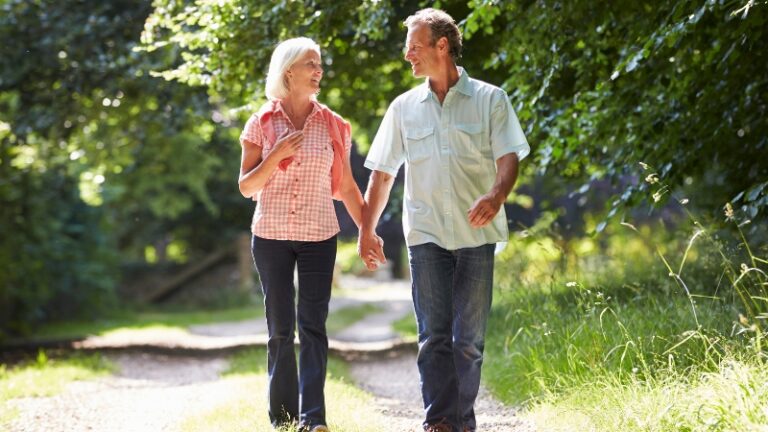 Older couple walking hand in hand on a forest path, showing connection and support during menopause