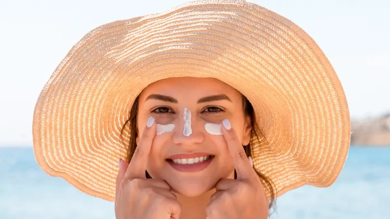 Woman applying sunscreen on her face at the beach as part of her skincare routine during a family vacation
