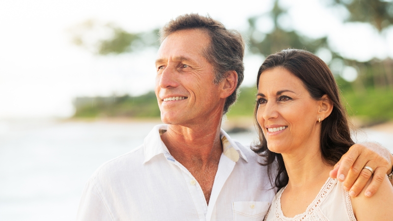 A middle-aged couple standing together on the beach, smiling and showing closeness during menopause