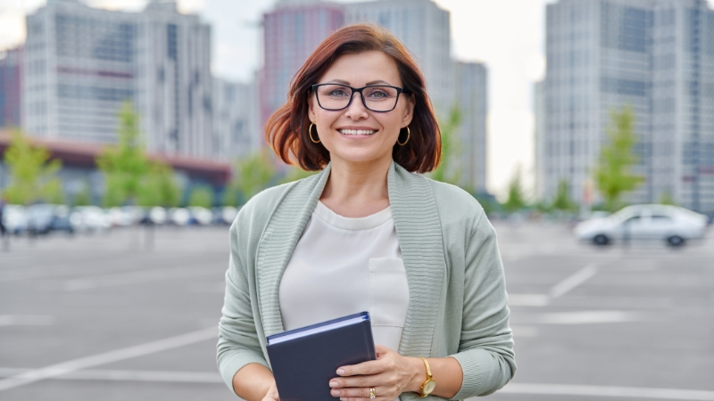 A confident woman with glasses holds a notebook