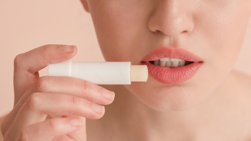 A woman applies lip balm, highlighting concerns about mineral oil and paraffin in skincare products