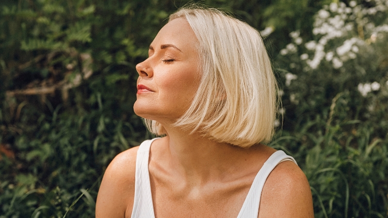 A woman with short blonde hair sits outdoors with closed eyes