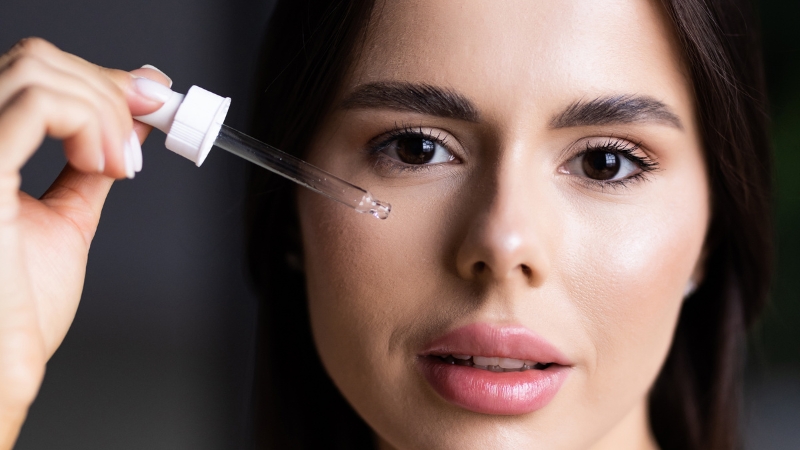 A woman holds a dropper near her face, demonstrating a smell test to check if niacinamide serum has expired