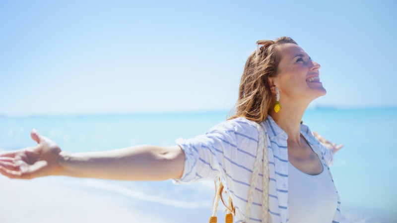 A happy woman stands on the beach with open arms, showing style and self-expression after 40