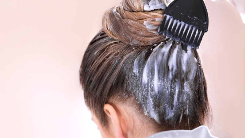 Person applying creamy hair dye to the roots with a brush, showing how hair dye saturates the scalp area during coloring