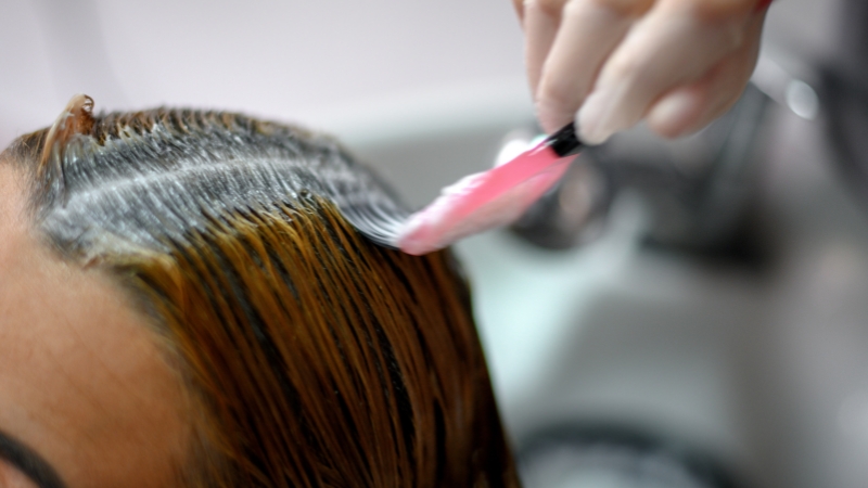 Person rinsing hair dye at a salon sink to remove excess product after coloring