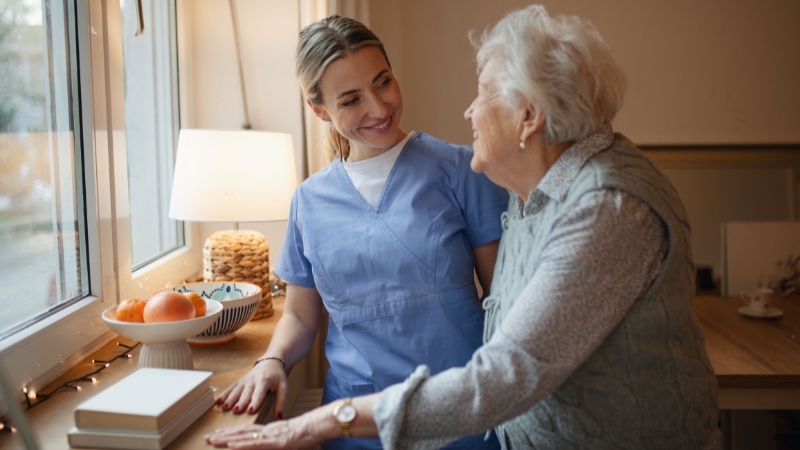 A nurse smiles while supporting an elderly woman at home, highlighting care during early dementia symptoms