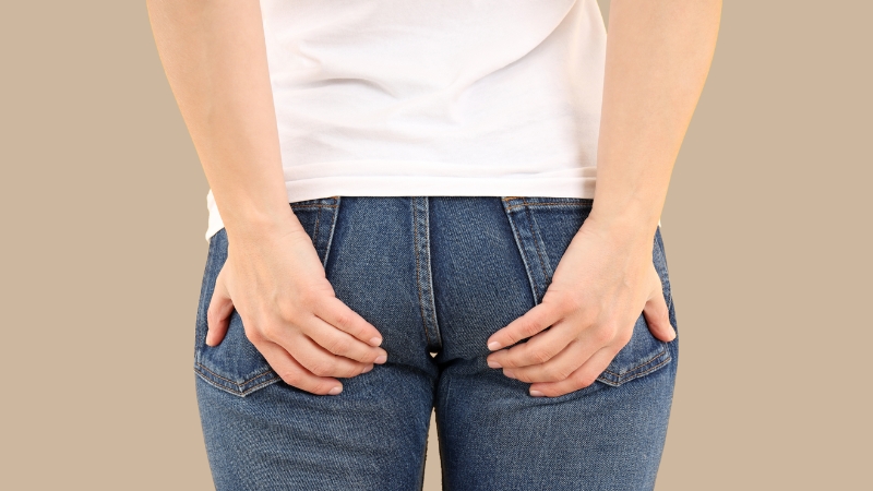 A woman in jeans places her hands on her lower back, illustrating the focus area of a Miami Thong Lift