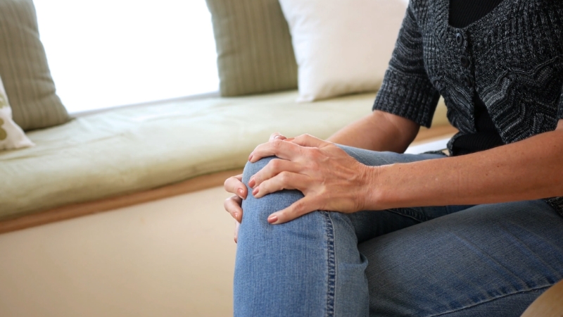 A person sits holding their knee at home, reflecting common health focus after 50