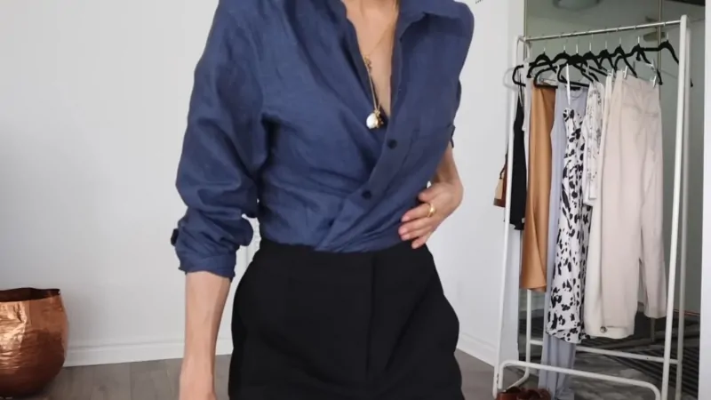 A woman styles a blue button-up shirt with black trousers in a capsule wardrobe outfit