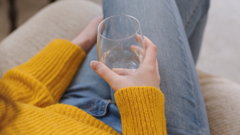 A mother sits relaxed on a couch holding a glass of water in her hand