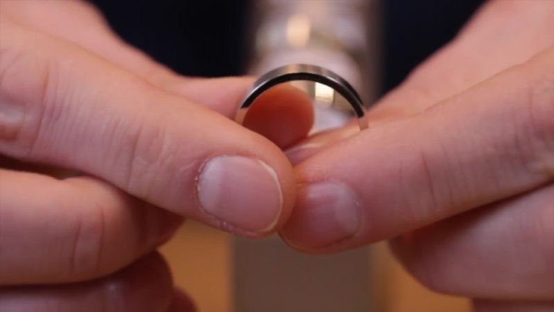 A person holding a polished palladium ring between their fingers in a close-up shot
