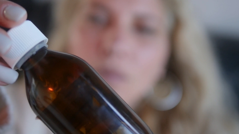 A woman examines a supplement bottle label up close before use