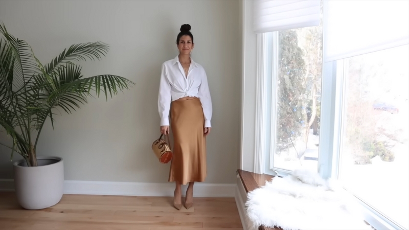 A woman wears a white shirt styled with a gold satin slip skirt and heels