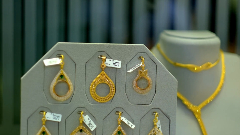 Gold earrings displayed on a jewelry stand next to a matching necklace on a mannequin