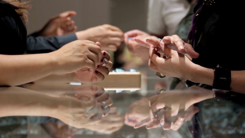 People trying on rings at a jewelry counter with hands reflected on the glass surface