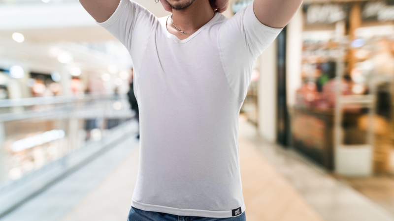 Man wearing a white undershirt with visible underarm sweat protection panels in a public indoor space