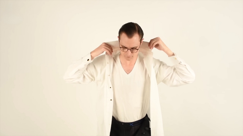 Man putting on a dress shirt over a white undershirt against a light background