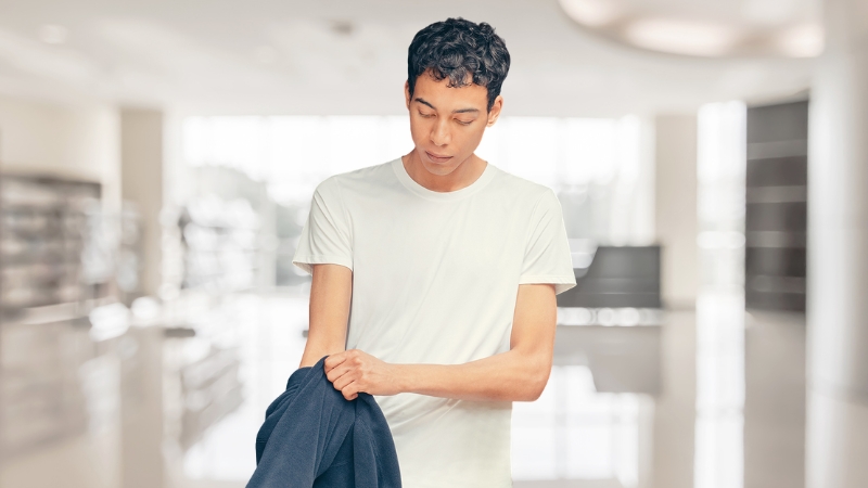 Man wearing a white undershirt while holding a jacket in a bright indoor setting