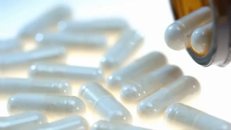 Close-up of biotin supplements capsules spilled from a brown bottle onto a white surface