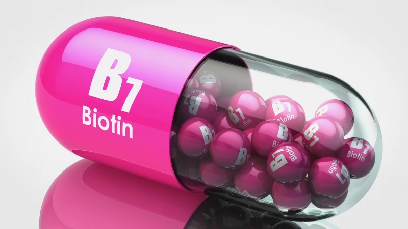 Pink capsule labeled B7 Biotin filled with small biotin tablets on a white background