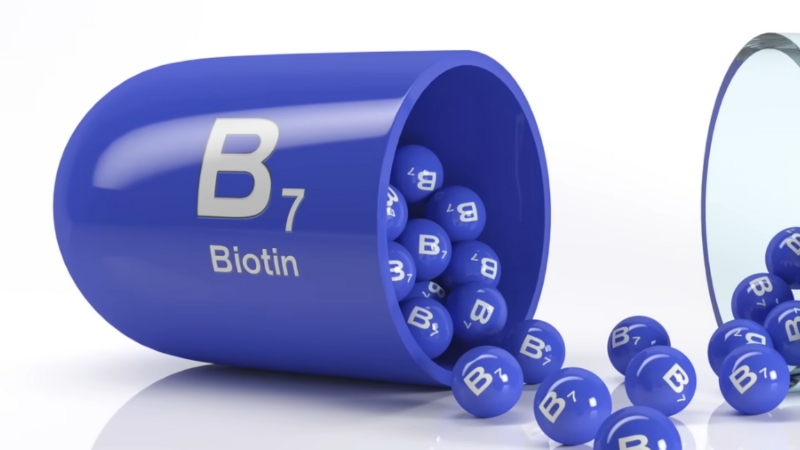 Blue capsule labeled B7 Biotin spilling small biotin tablets onto a white surface
