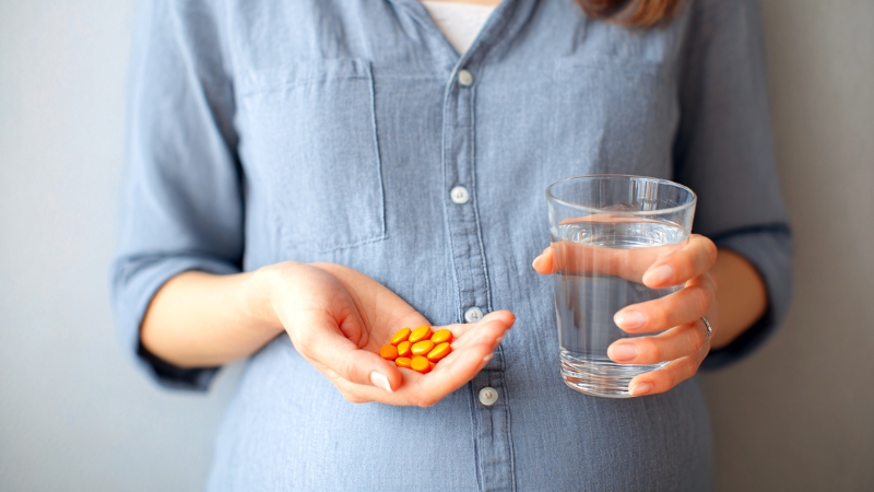 Pregnant woman holding orange supplement pills in one hand and a glass of water in the other