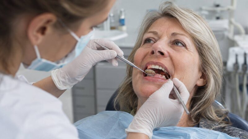 Dentist examining the gums of a woman over 50 during a dental checkup.